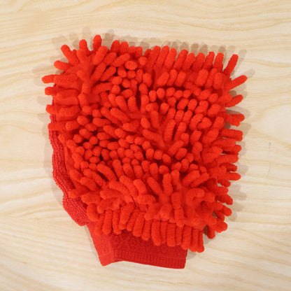 A red microfiber chenille wash glove, with a textured surface, rests on a light wooden surface.