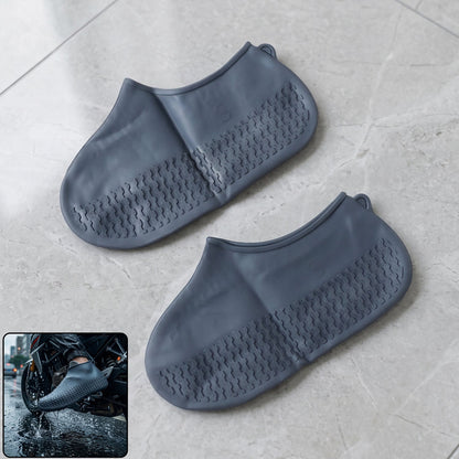 A pair of dark gray silicone shoe covers with textured soles rests on a light gray tiled floor, with an inset of a person