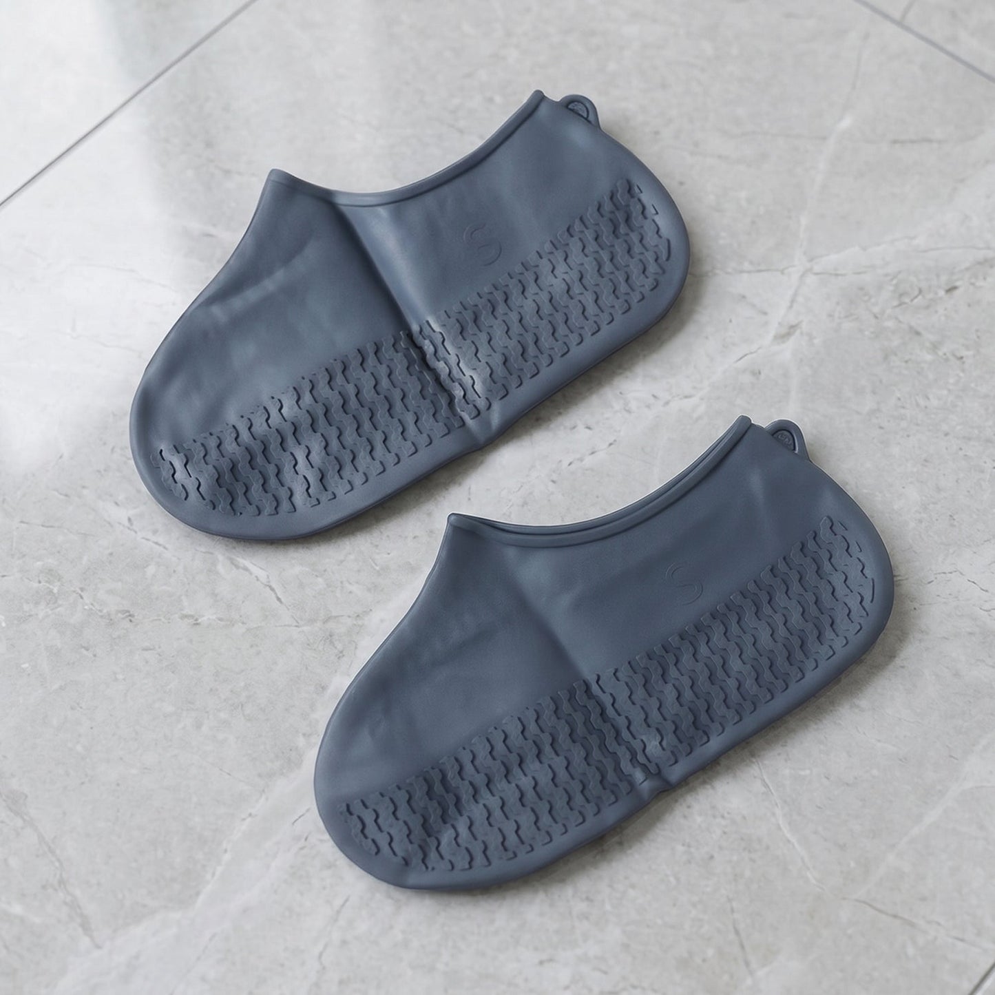 Two navy blue silicone shoe covers are laid flat on a light grey tiled surface, showcasing their textured soles.